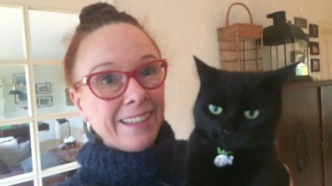 En kvinna med glasögon och en svart katt. Katten ser ut som en gammal katt som skriker.