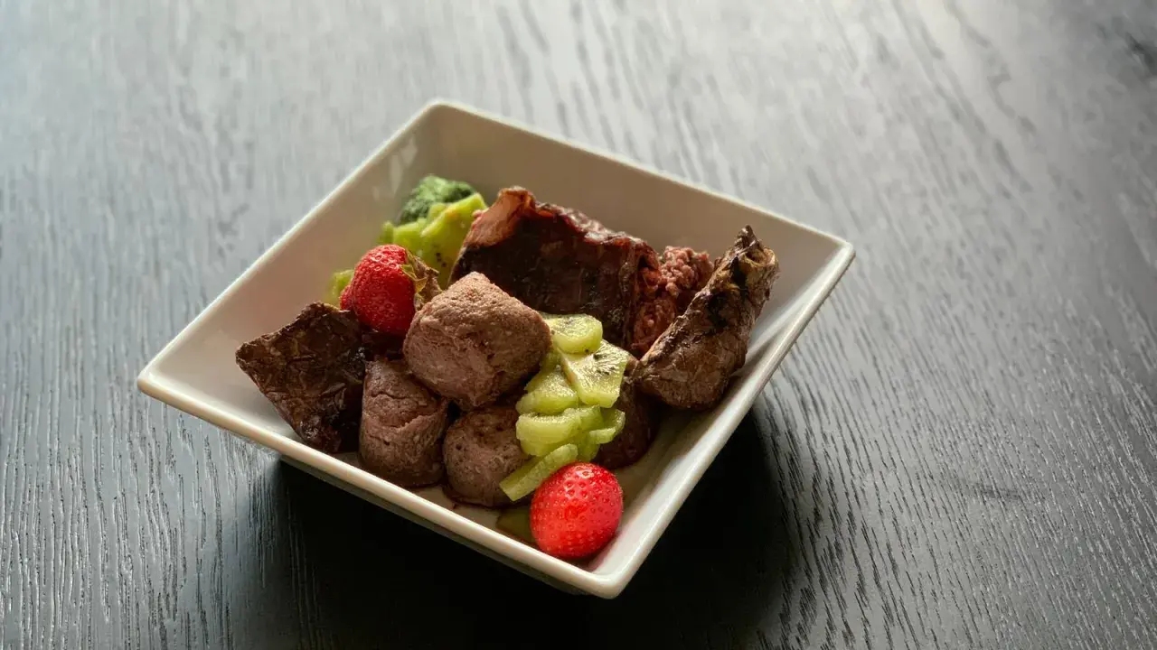 En skål med matberikning för hund: köttbitar, kiwi och jordgubbar. En näringsrik och god måltid för din fyrbenta vän.