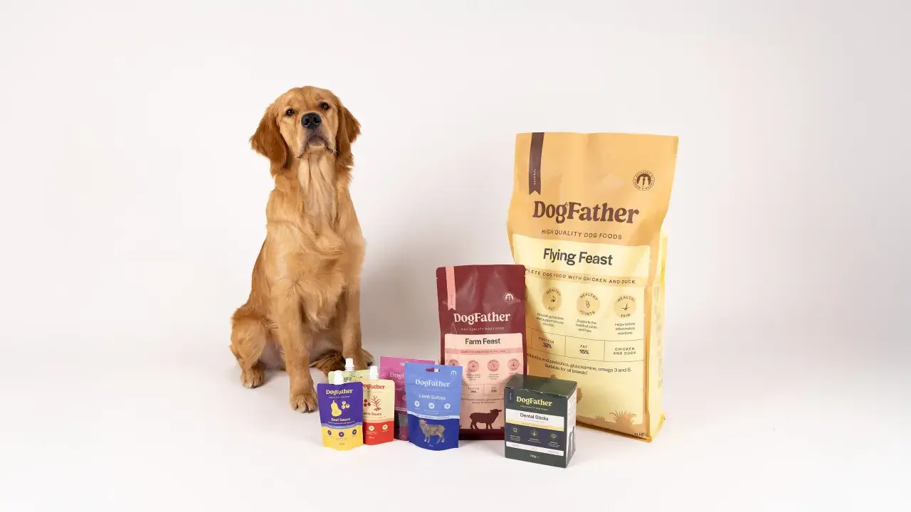 Golden retriever sitter bredvid DogFather-foder. Förpackningar med foder till hund som fiser, som "Flying Feast" och "Farm Feast", samt godis och såser.