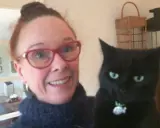En kvinna med glasögon och en svart katt. Katten ser ut som en gammal katt som skriker.