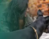 En kvinna med mörkt hår och kamouflagejacka visar sitt ledarskap hund vid en vattensamling.