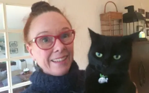 En kvinna med glasögon och en svart katt. Katten ser ut som en gammal katt som skriker.