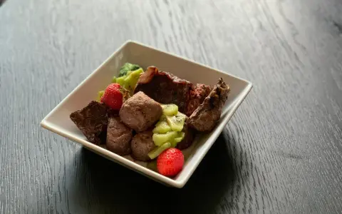 En skål med matberikning för hund: köttbitar, kiwi och jordgubbar. En näringsrik och god måltid för din fyrbenta vän.