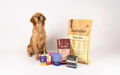 Golden retriever sitter bredvid DogFather-foder. Förpackningar med foder till hund som fiser, som "Flying Feast" och "Farm Feast", samt godis och såser.