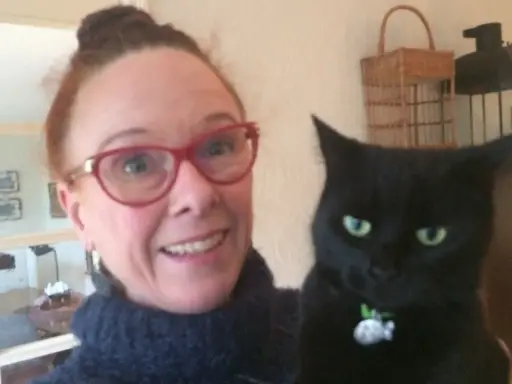 En kvinna med glasögon och en svart katt. Katten ser ut som en gammal katt som skriker.