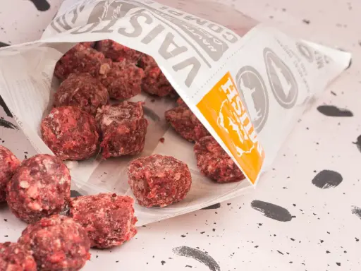 Fryst barf hundmat i form av köttbullar som vält ut ur en påse.